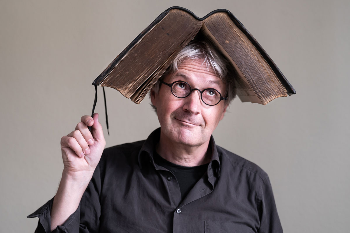 Jörg Hilbert mit aufgeschlagenem Buch auf dem Kopf